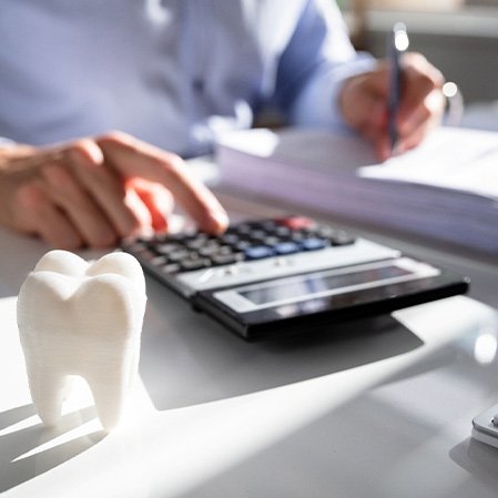 Someone sitting at desk writing with model tooth writing on paper pressing calculator