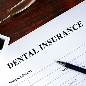 Closeup of dental insurance form with pen, glasses, money, and dental X-rays