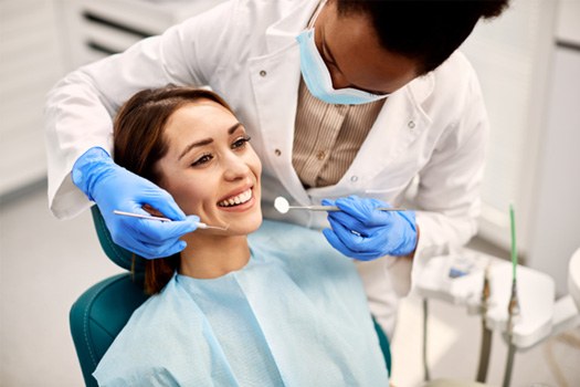 Woman in dental chair about to undergo exam by dentist in blue gloves
