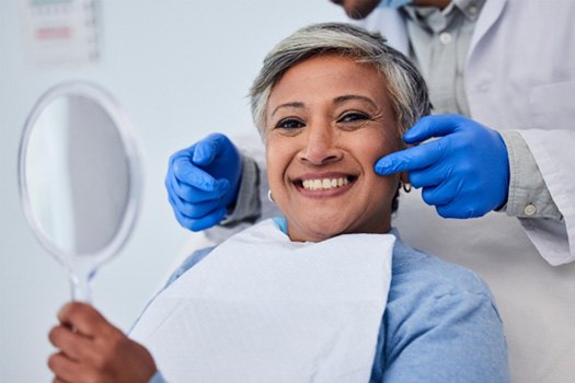 Woman in dental chair smiling holding mirror with dentist pointing to her cheeks