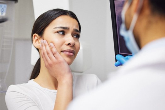Woman holding hand to cheek in pain looking at X-rays with dentist
