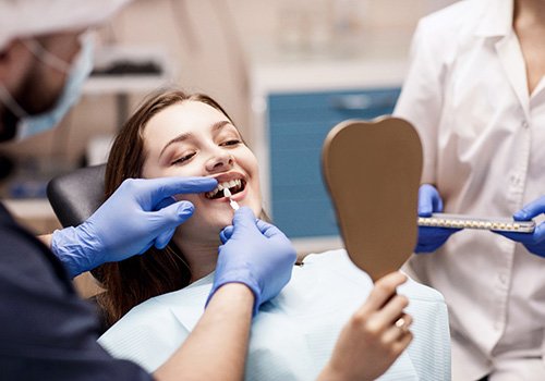 Woman looking in mirror as dentist holds shade guide to her teeth