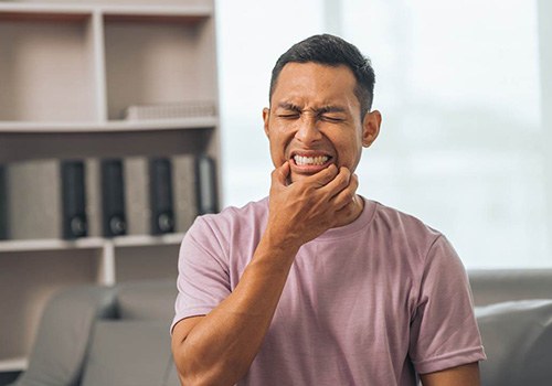 Man in pink shirt squinting and squeezing jaw in pain